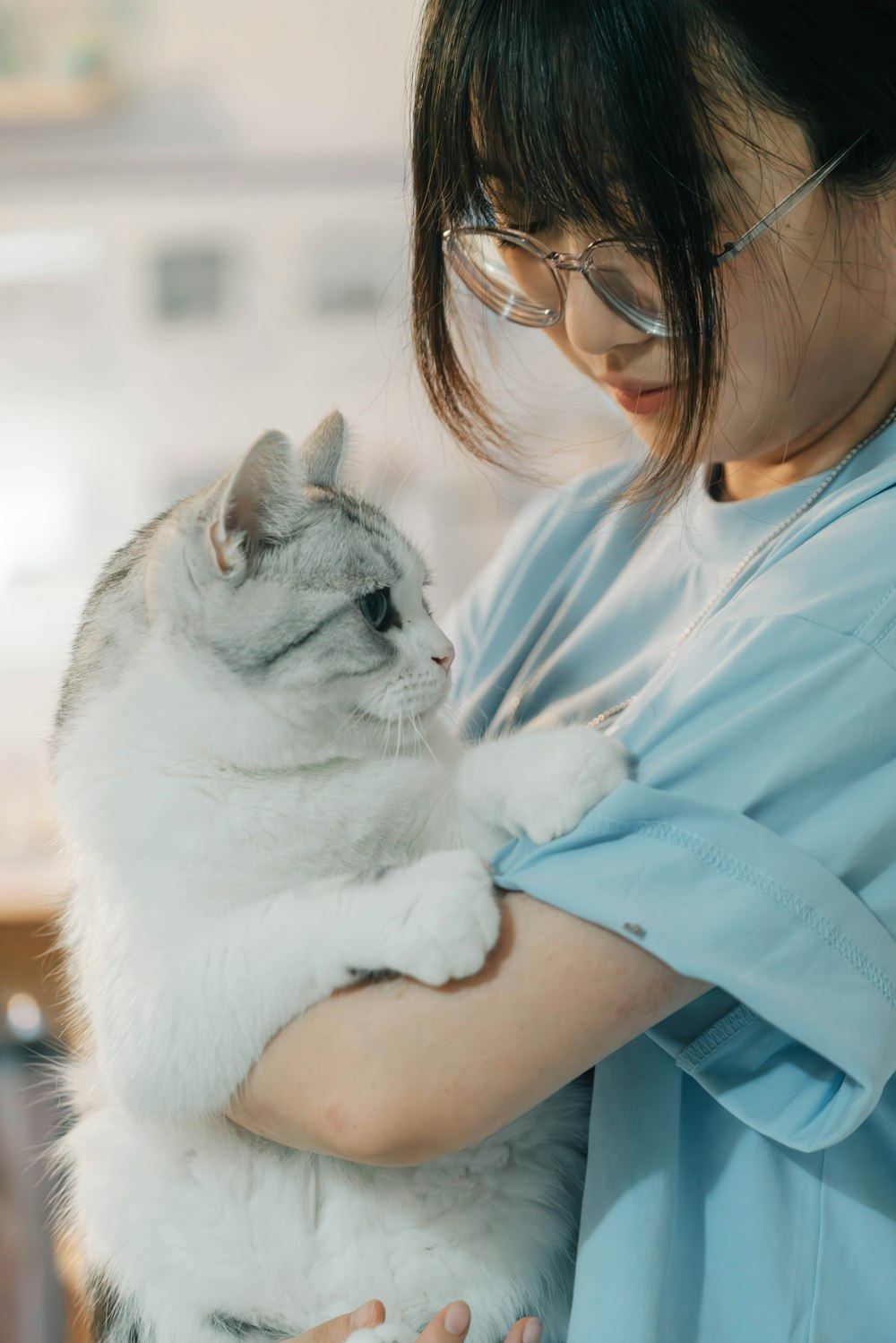 A veterinary technician in glasses holding a grey and white cat