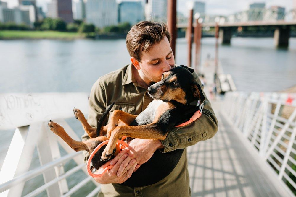 A man in a brown jacket hugging his dog on a boardwalk