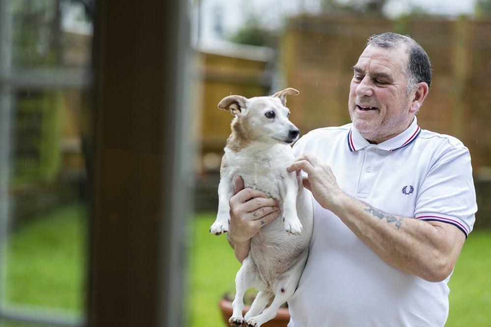 An older man smiling as he holds a small white dog