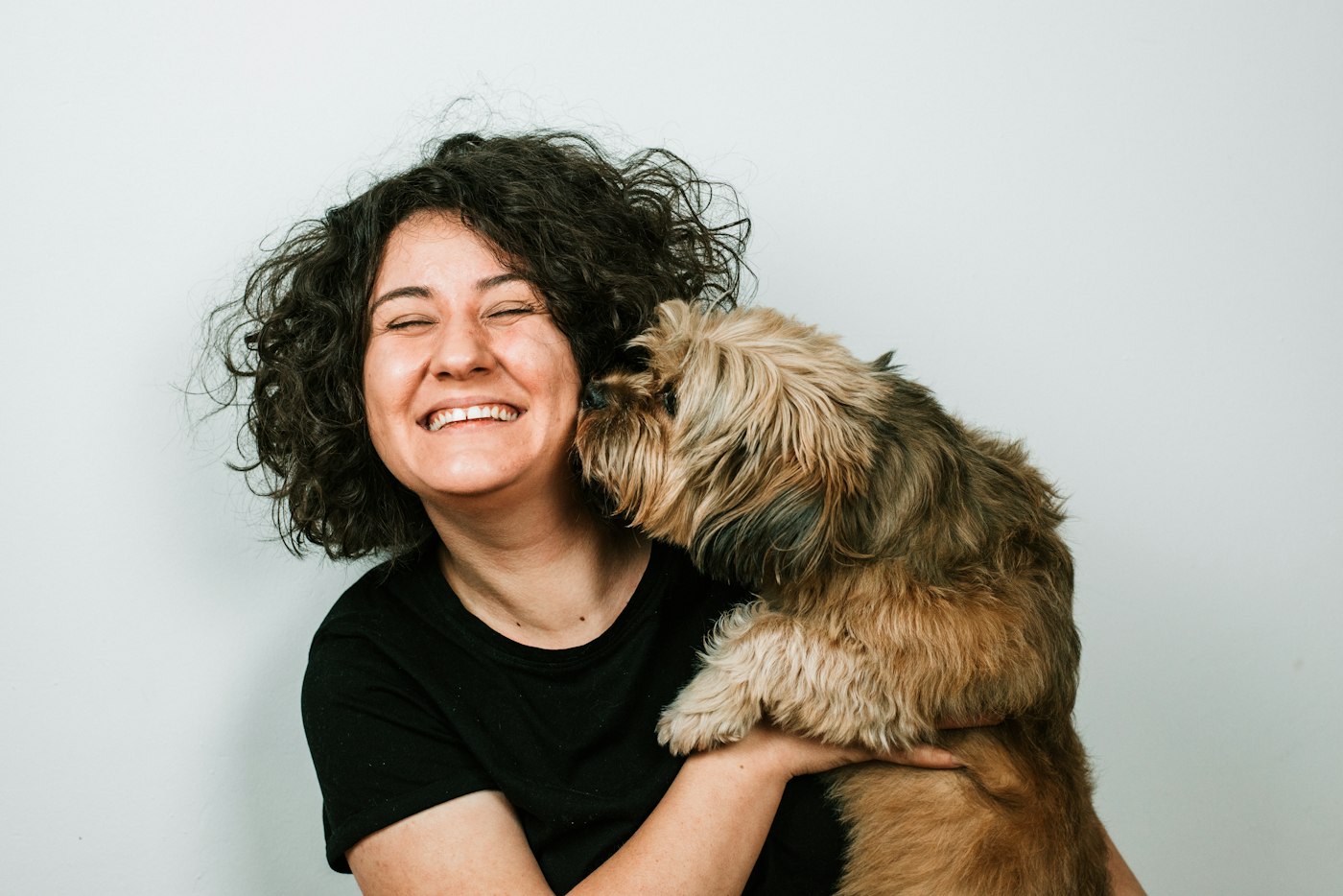 A woman laughing as her dog leans in to kiss her