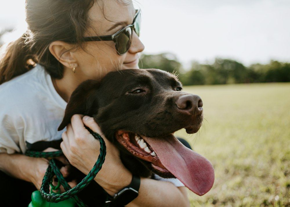 A woman in sunglasses hugging her happy brown dog outdoors